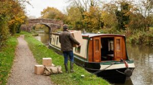 Narrowboat with wooden cabin doors open as belongings are carried aboard from the towpath